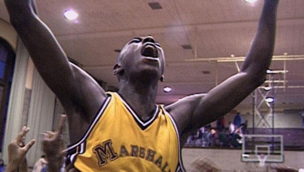 a Black man in a yellow jersey raises his hands to the sky