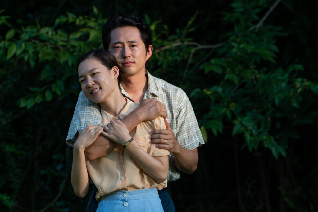 Asian couple embraces, both facing the camera, in front of a tree.