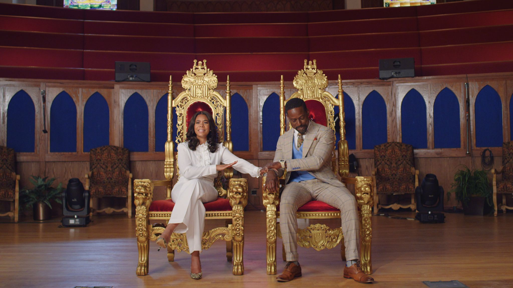 A dressed-up Black couple sit in side-by-side gold and red velvet thrones