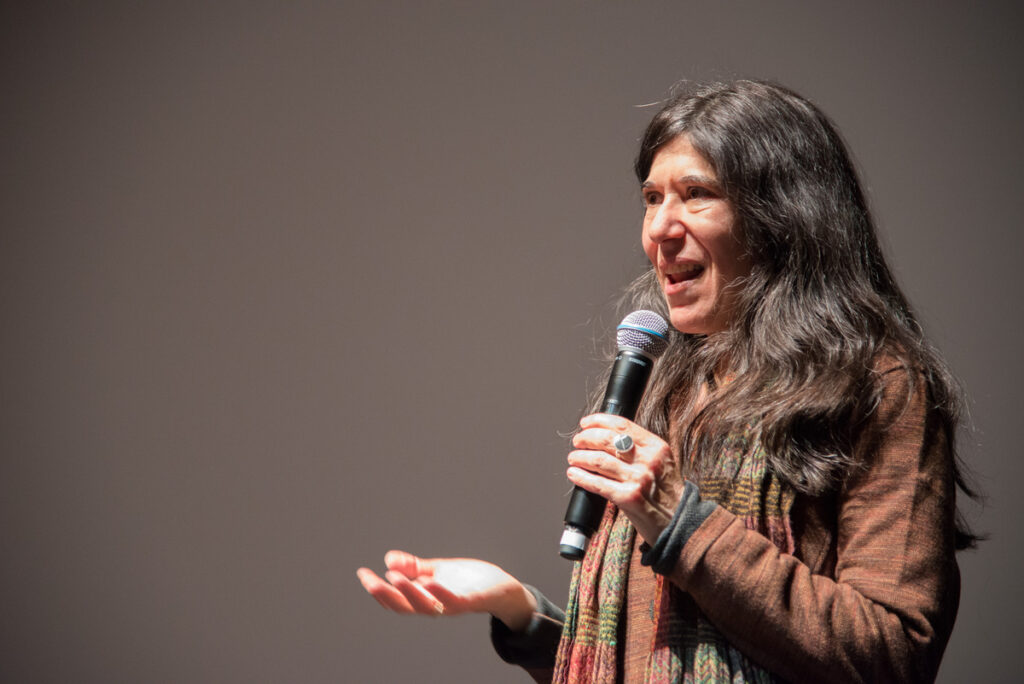 A woman holding a microphone addresses an audience.