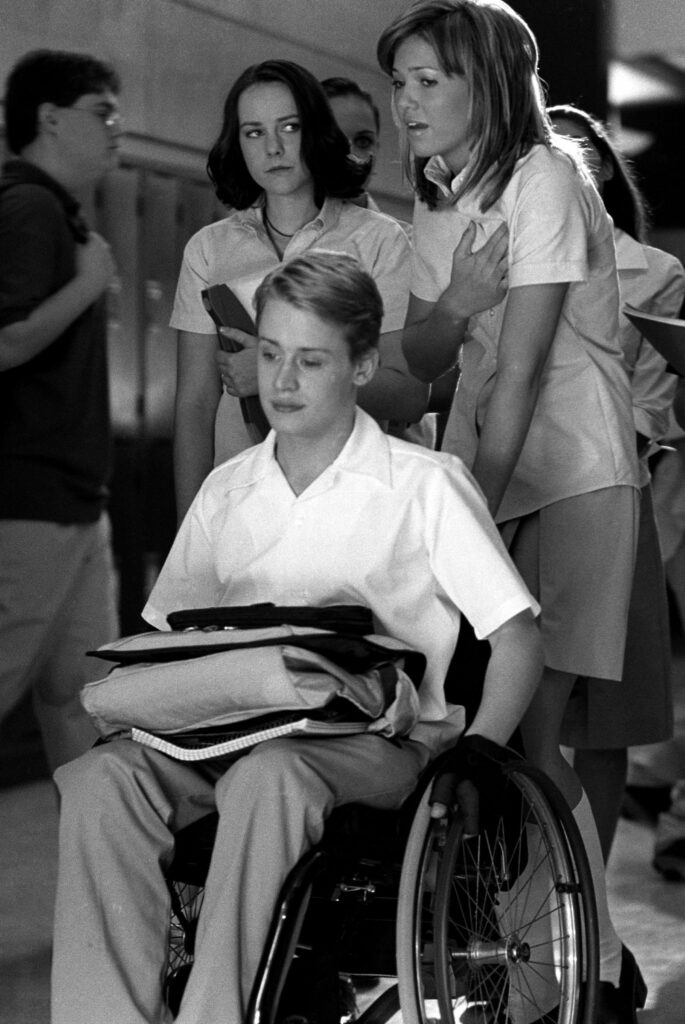 Young man sits in a wheelchair, with two young women behind him