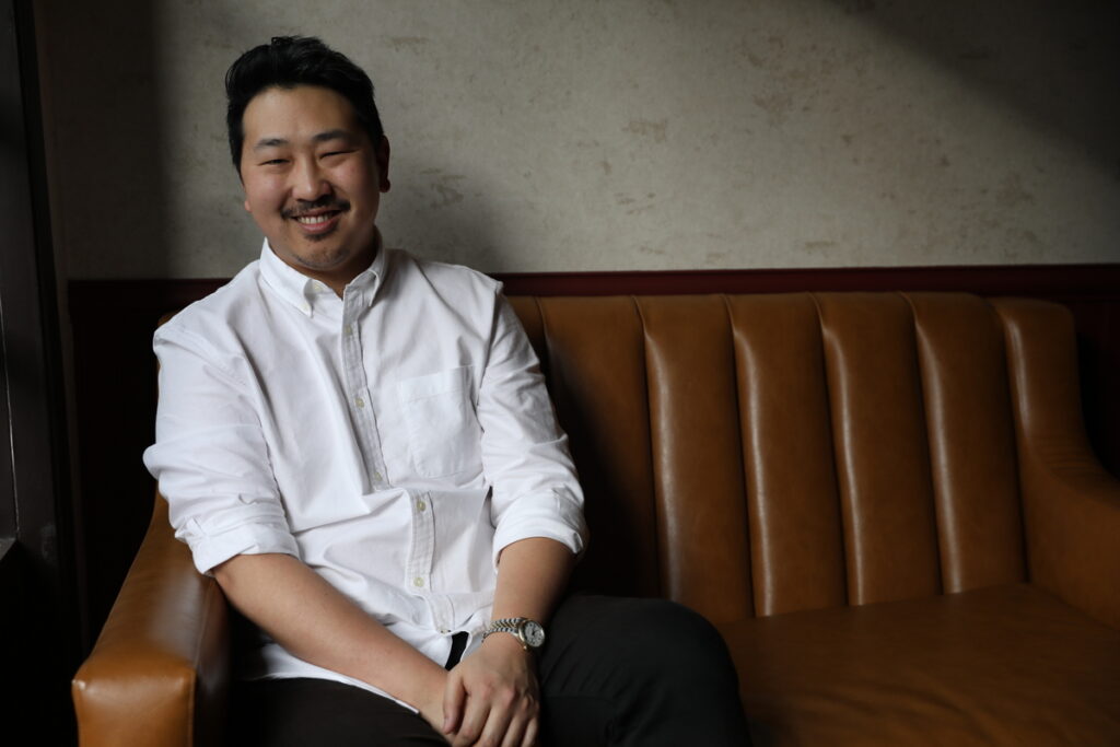 Asian man with moustache, sitting on a couch and smiling