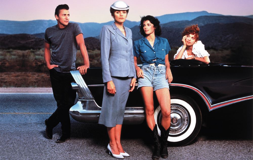 One man and three women pose with a 1950s vehicle