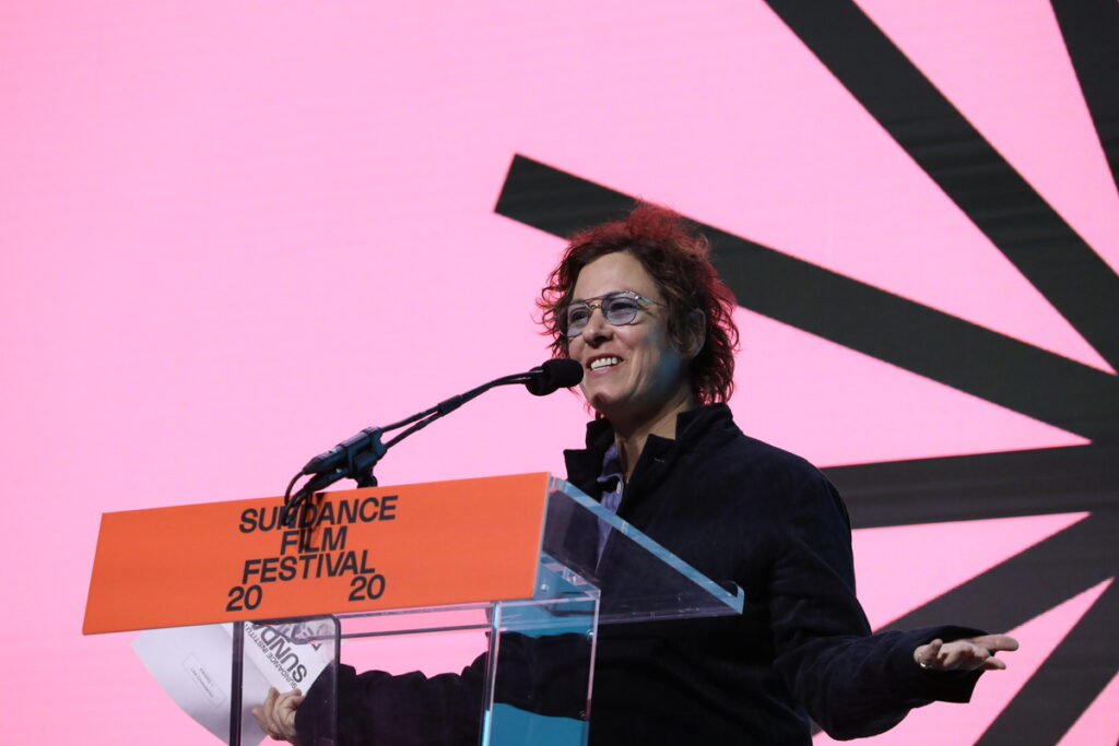 Smiling woman stands in front of a 2020 Sundance Film Festival podium