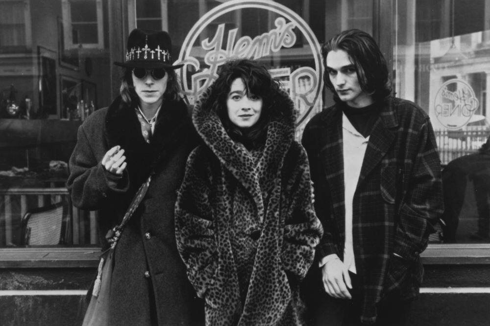 Three people (two men and a woman) stand before a storefront in this black and white photo.