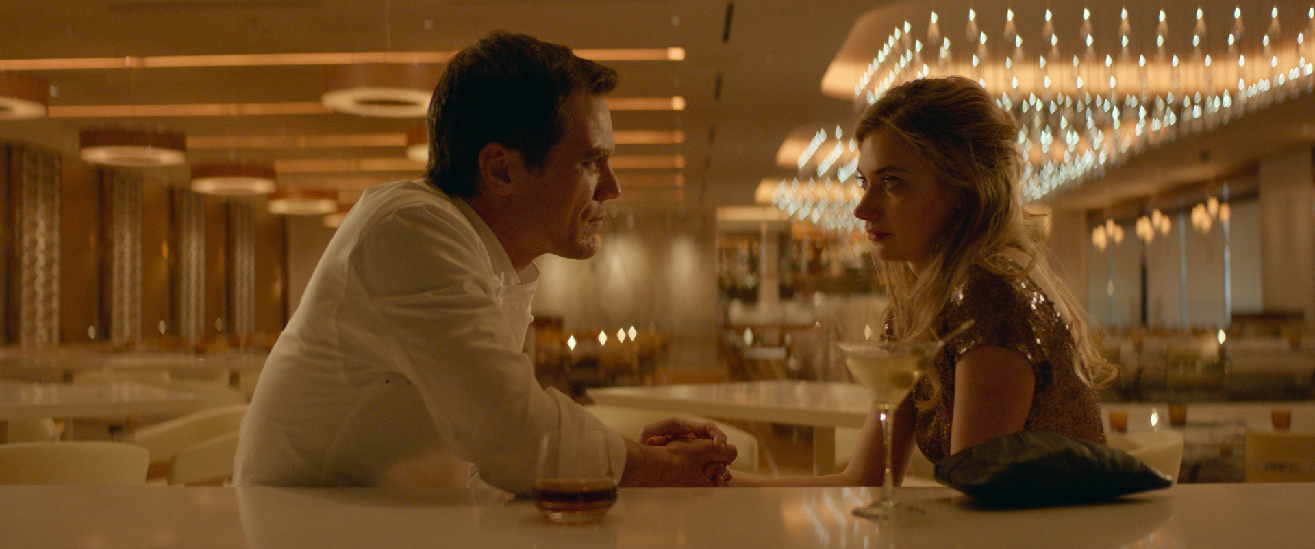 A young, brown-haired man in a white shirt sits holding hands with a blonde woman at a casino in Las Vegas.