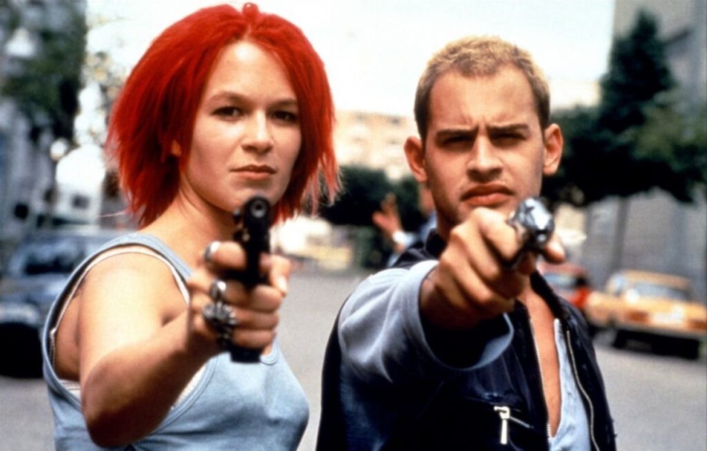Woman and man standing side-by-side and pointing pistols at the camera