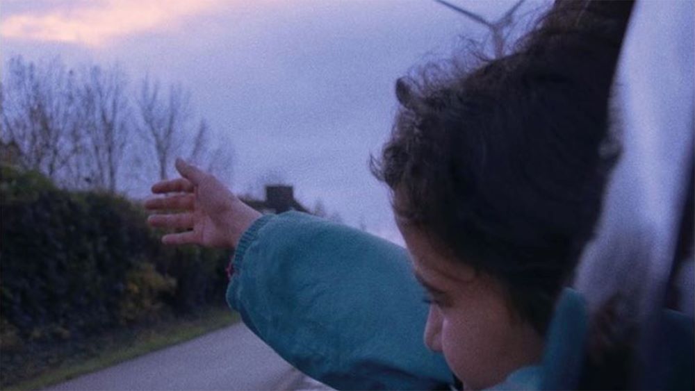 Child leans out of car window to feel the breeze on her hand