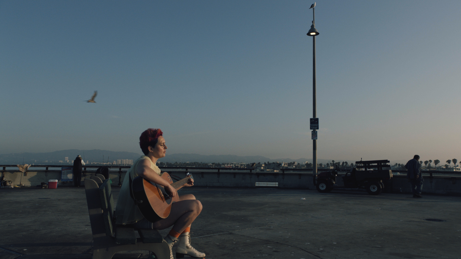 A young man sits at a bench as he plays the guitar