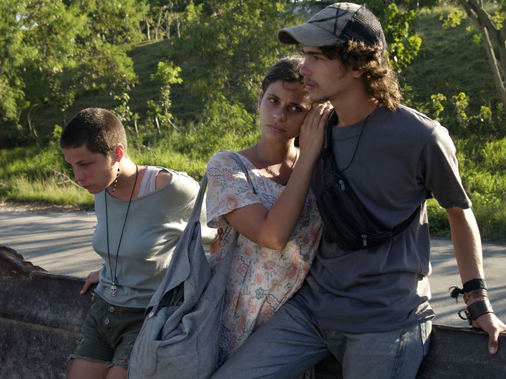 Two short-haired young women and a young man with long hair and a ball cap,lean against a short wall.