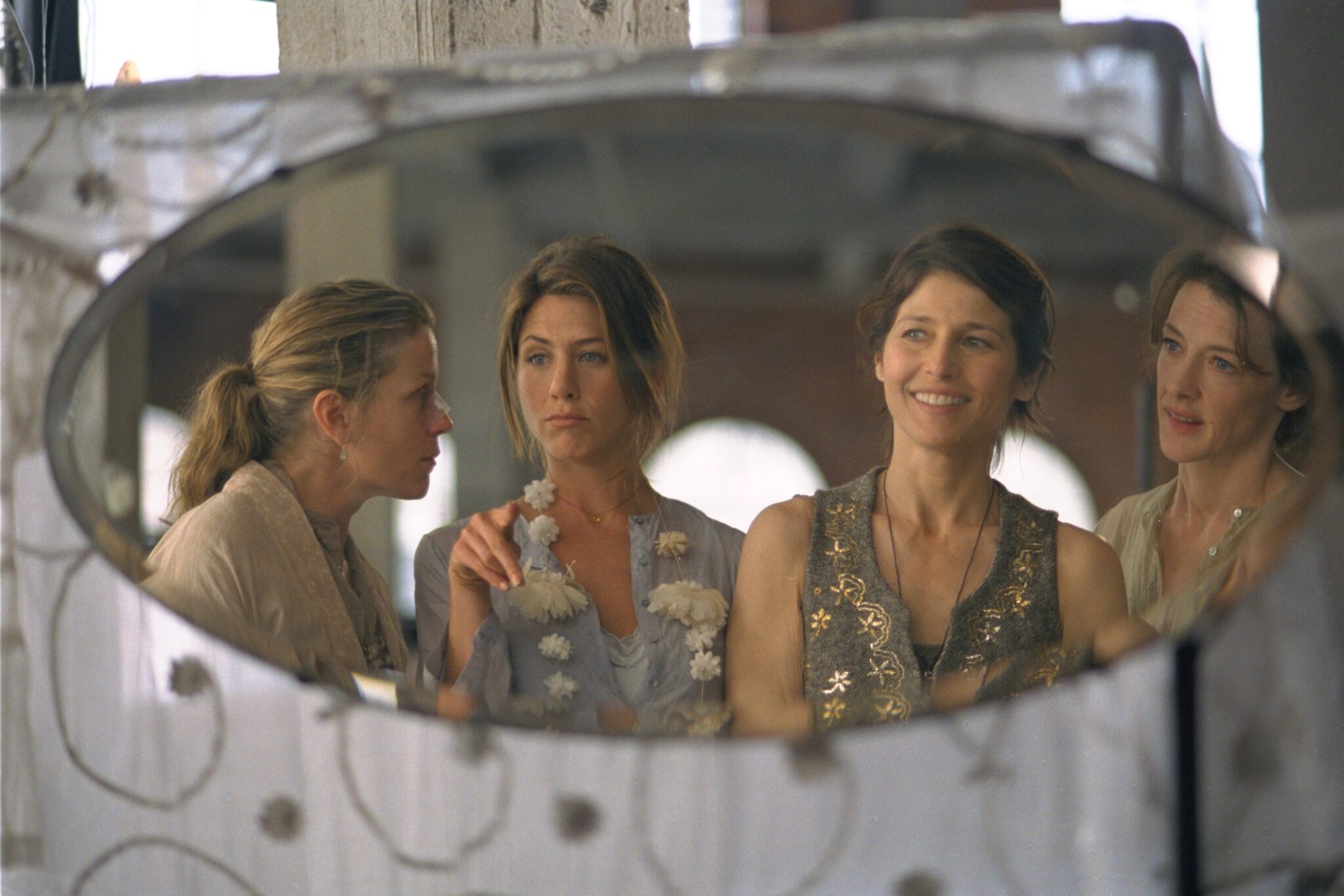 Four women stand in front of a round mirror chatting
