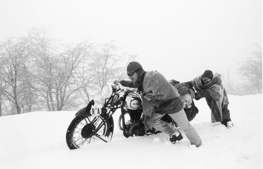 Two men push a motorcycle through snow