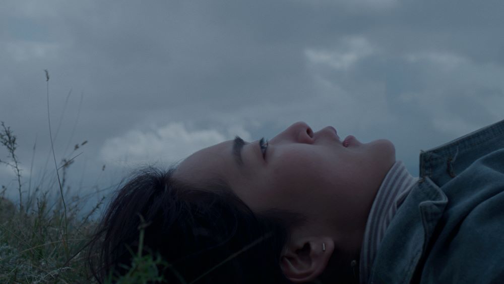 Side view of young Asian woman lying in grass under a cloudy sky