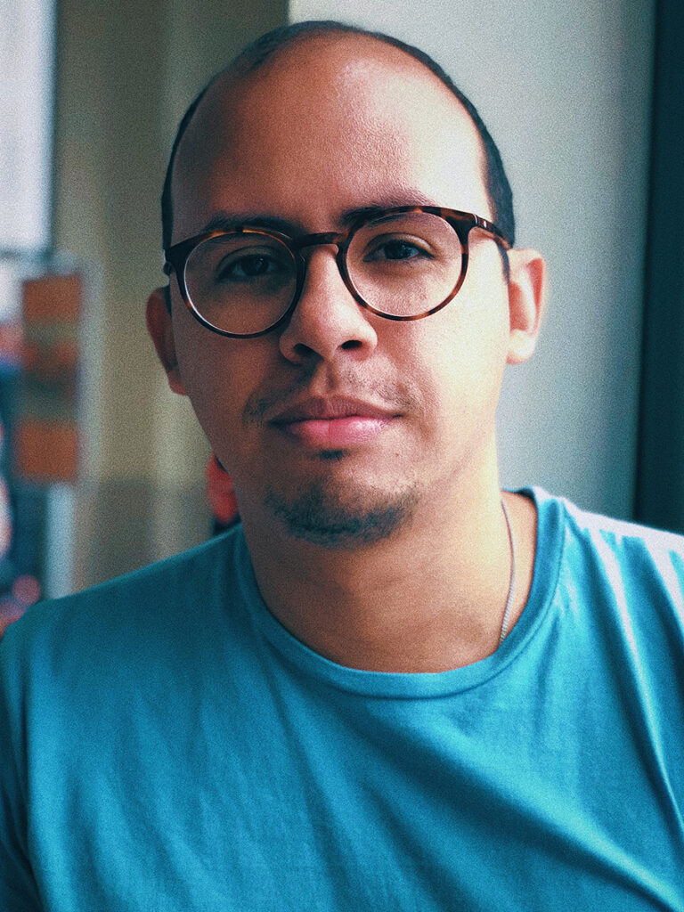 Balding man wearing eyeglasses, with a short goatee and moustache, in a blue T-shirt