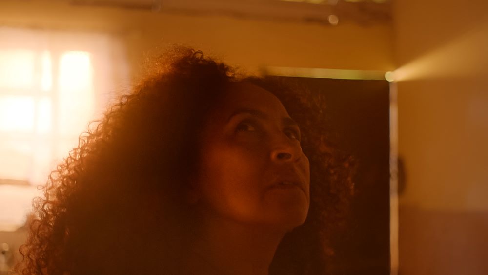Woman with cascading curly hair with face upturned in a room cast with yellow-orange light