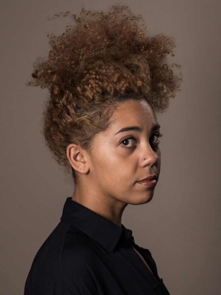 Woman with fuzzy brown Afro standing sideways with face turned toward camera