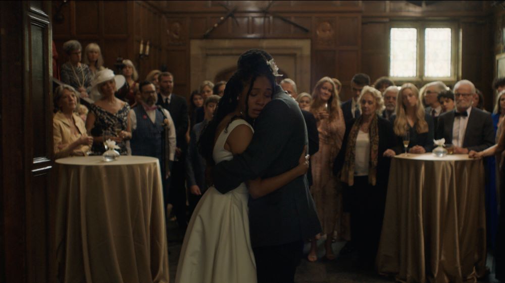 Couple in formal attire embracing, with crowd looking on