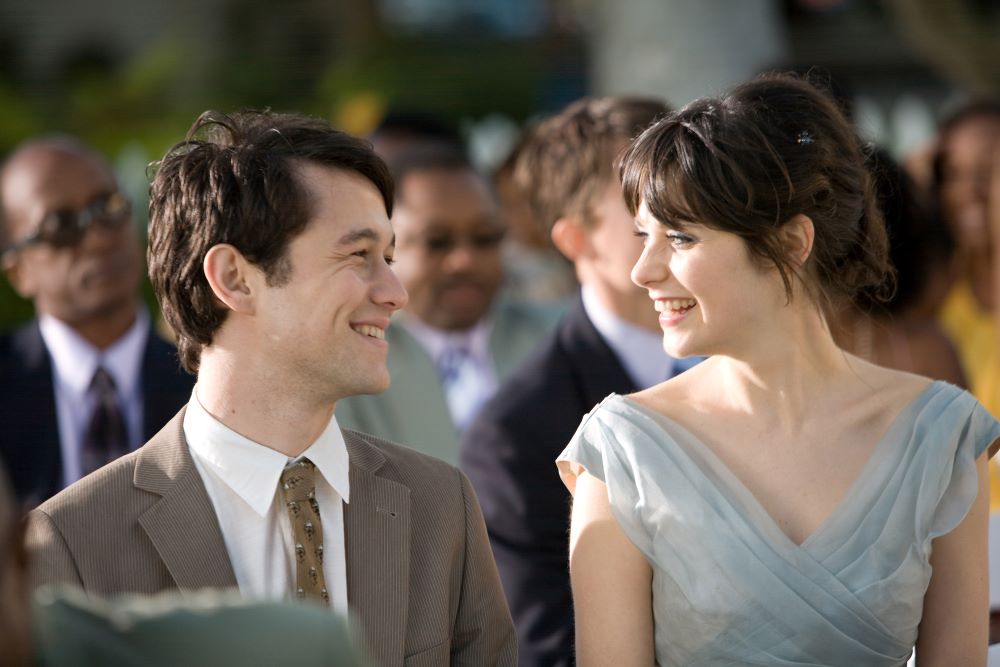 Young man in suit and young woman in formalwear smile at each other.