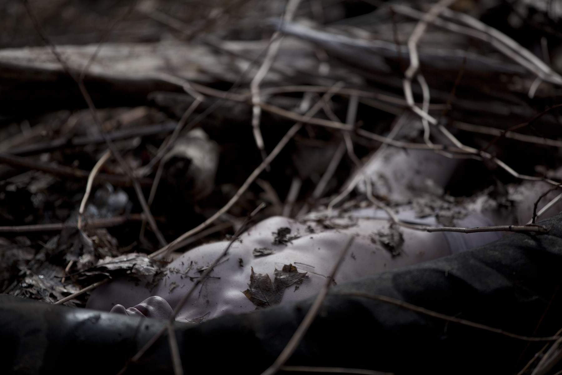 A deceased body lays on the floor covered in dirt and leaves