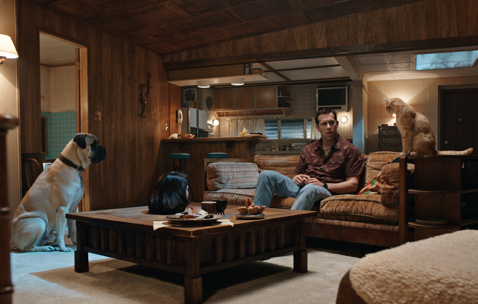 A man (Ryan Reynolds) sits on his couch looking at his cat and dog
