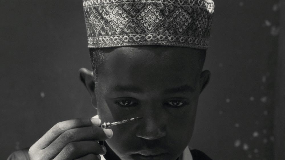 Young black person with decorative tribal hat applies paint to face