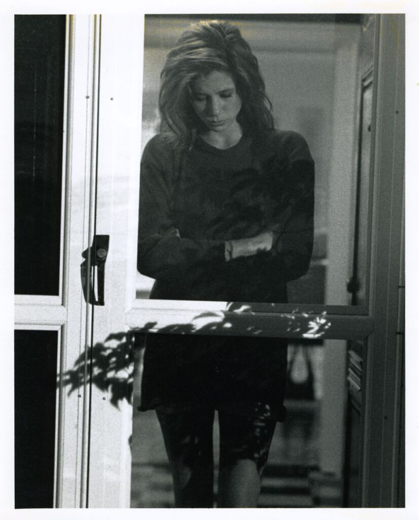 Young woman standing inside a screen door, looking down