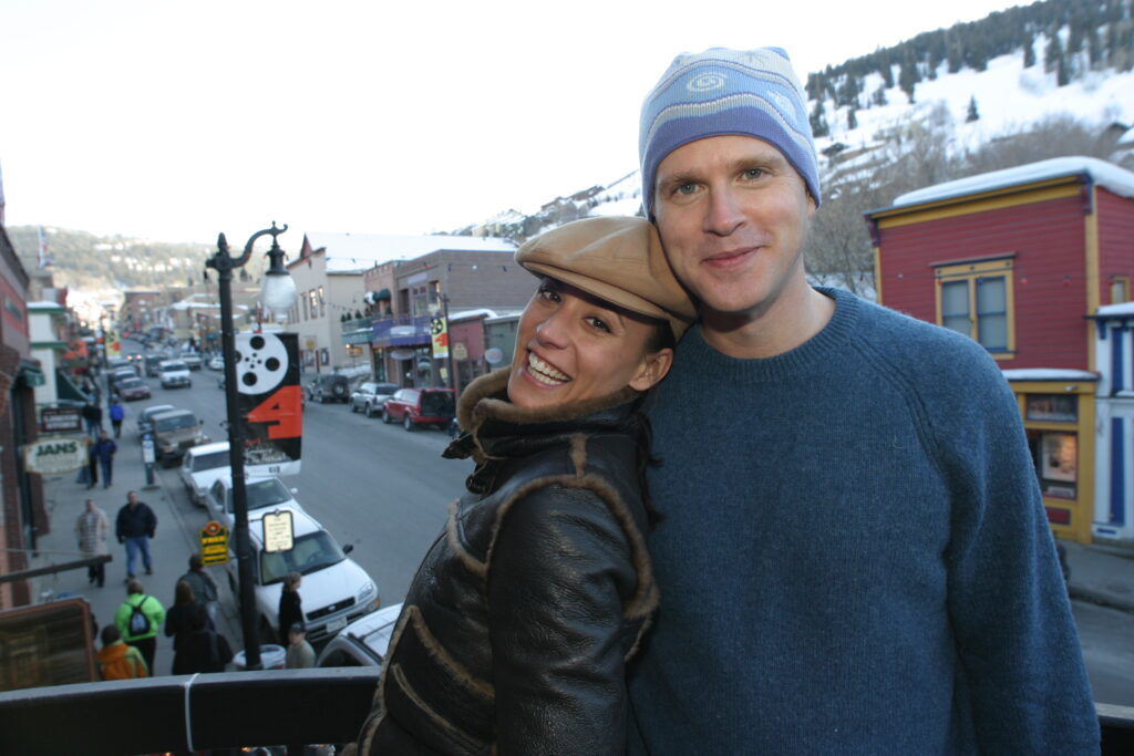 a man and a woman smiling at the camera on a balcony over the main street in Park City during Sundance