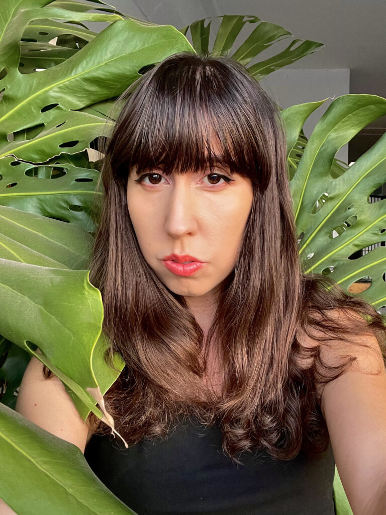 Native woman with bangs looking directly at the camera near bushes