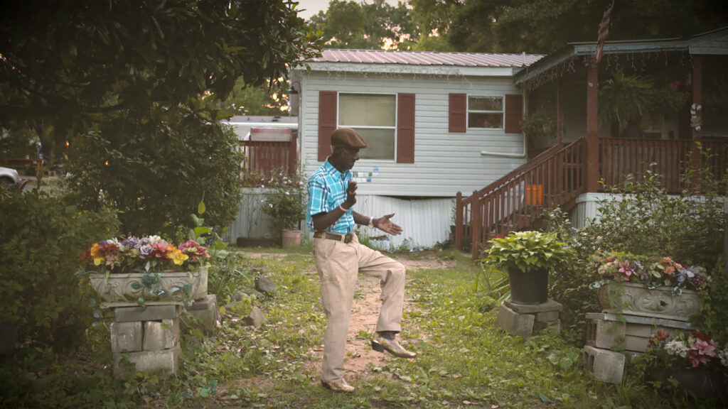 An elderly Black man dances in his front year