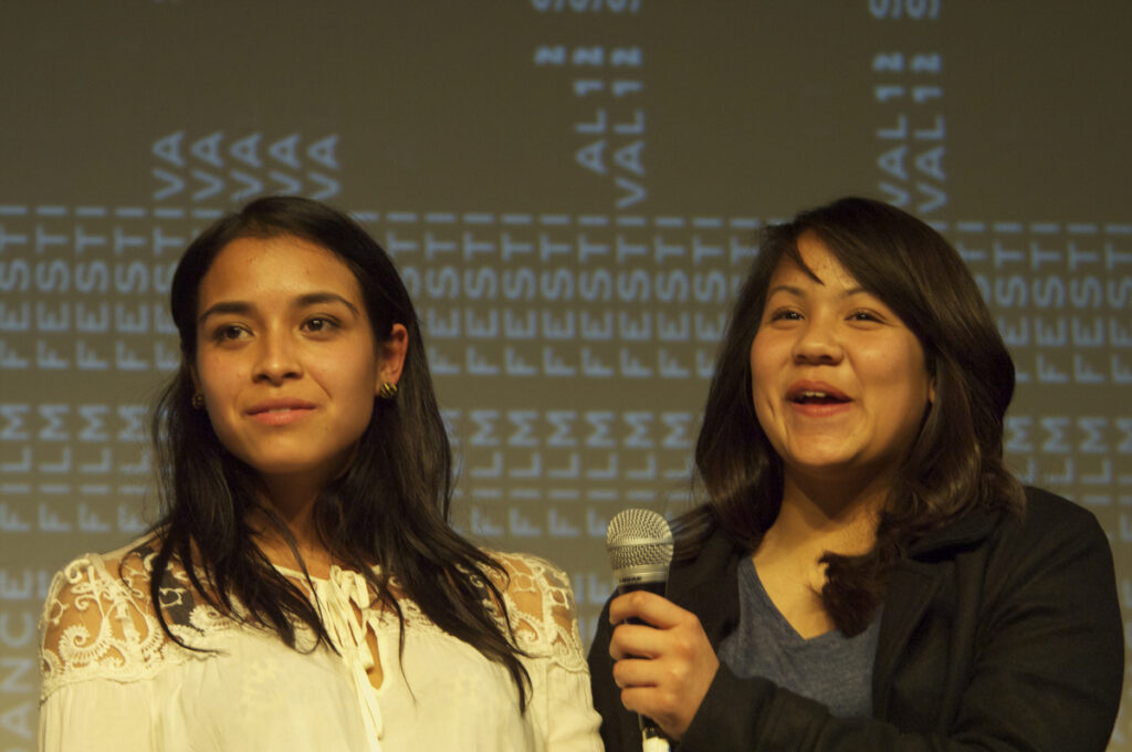 two women looking towards the camera, one talking with a microphone