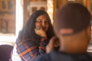 Stephanie smiles and intently listens to Brandon and resting her hand to her cheek with sunlight on her back