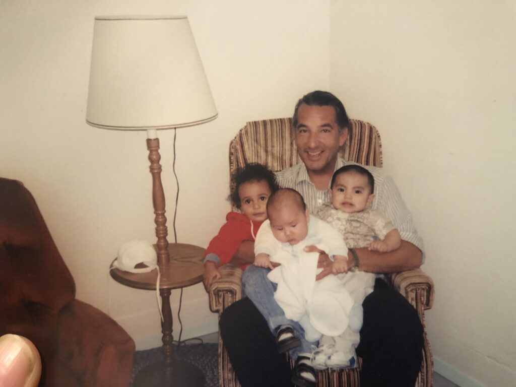 A man is sitting in an easy chair holding three small children including one baby looking at the camera