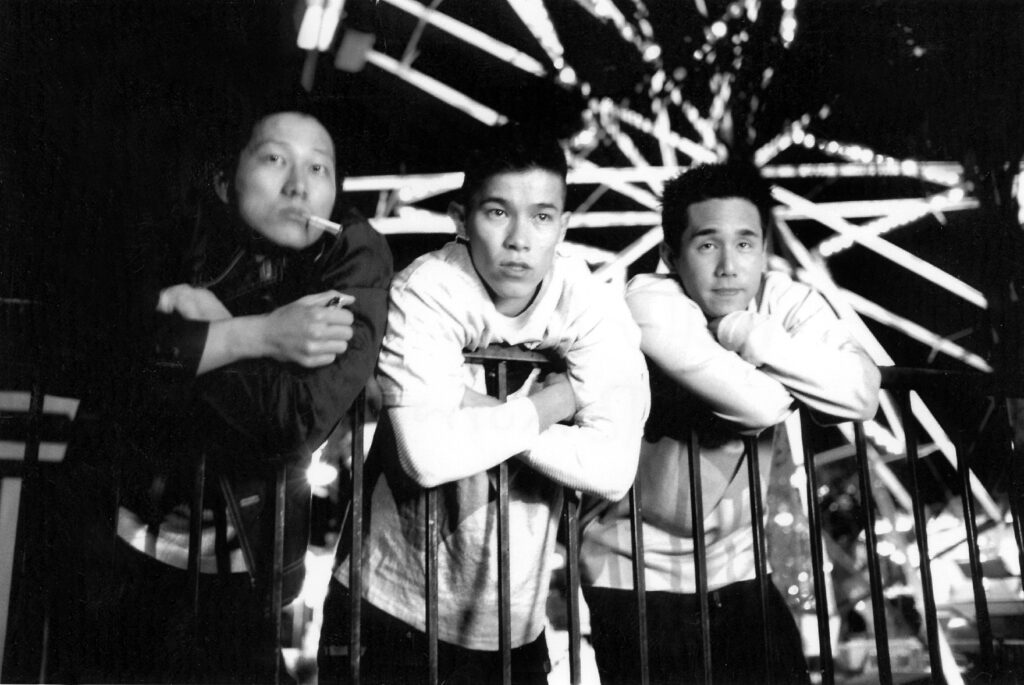 Three Asian men leaning on a banister in front of a ferris wheel