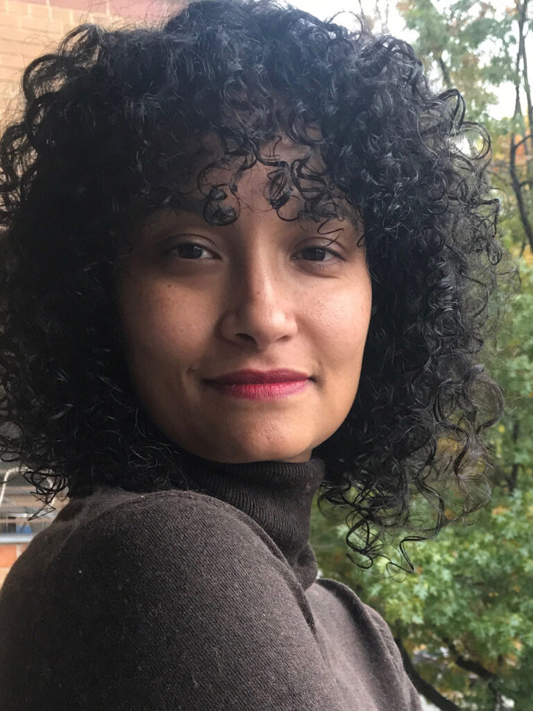 woman with curly hair smiling at the camera in a headshot