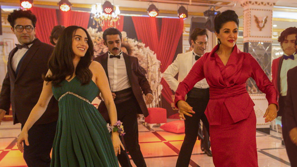 A Persian family dances at a family event. A young girl is wearing green and her mother is wearing red