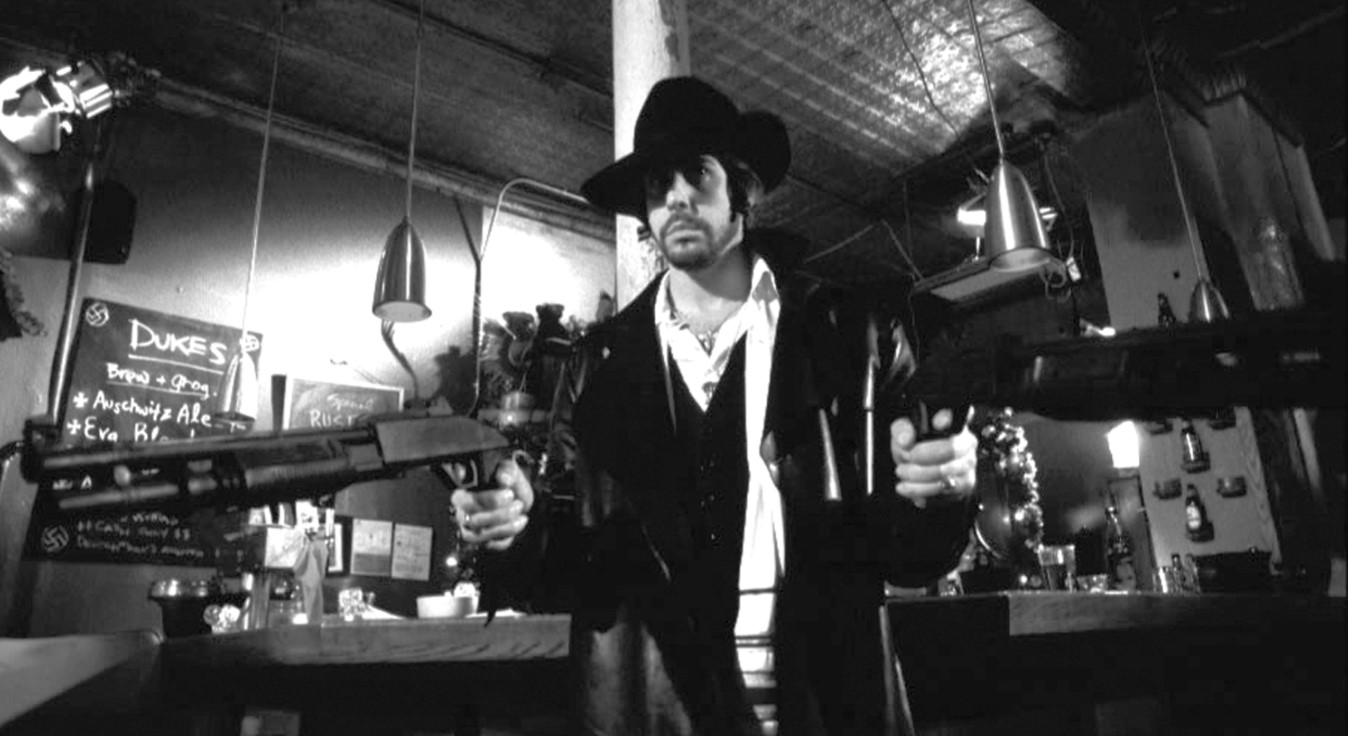 A black and white photo of a man holding two guns with CHristmas decor in the background