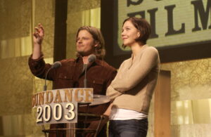 A man and a woman stand at a podium that says: Sundance 2003"