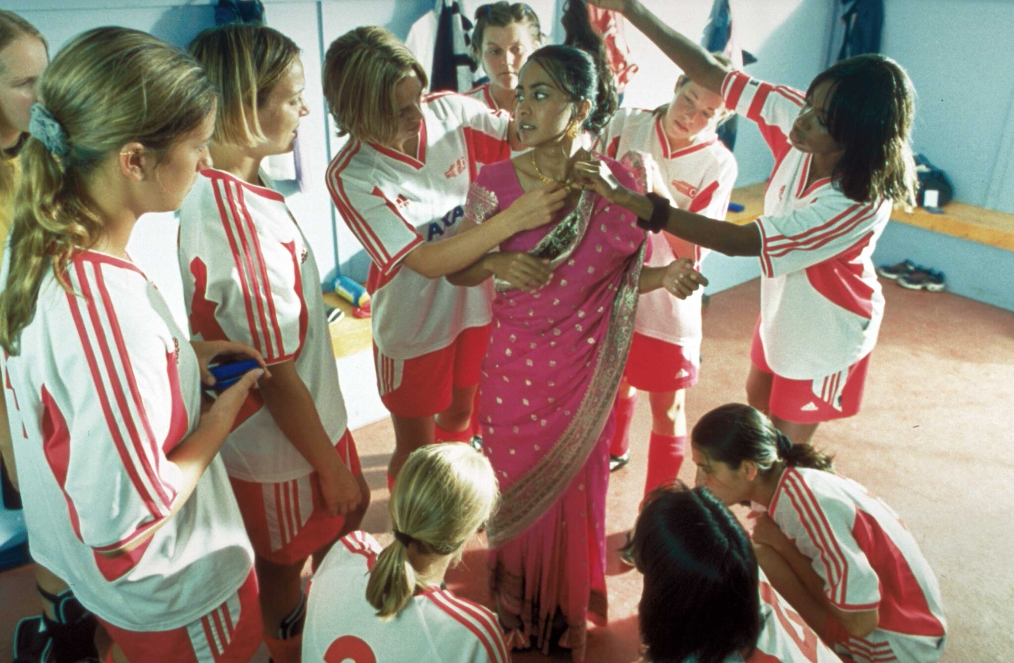 A group of teen soccer players surround a their teammate as they help her with her saree.