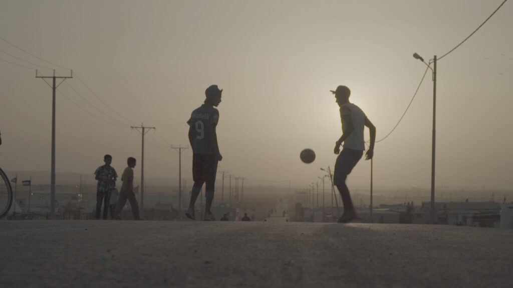 two men are playing soccer in the middle of the street, their bodies are in silhouette