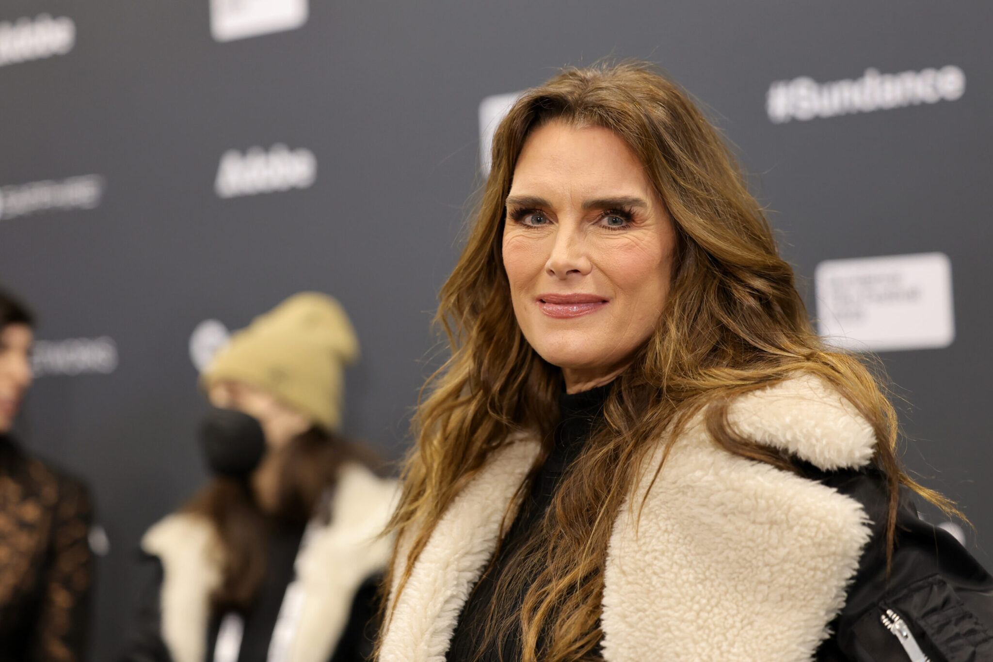 A woman (Brooke Shields) with long brown hair in a white and black coat smiles to the camera at the 2023 Sundance Film Festival.