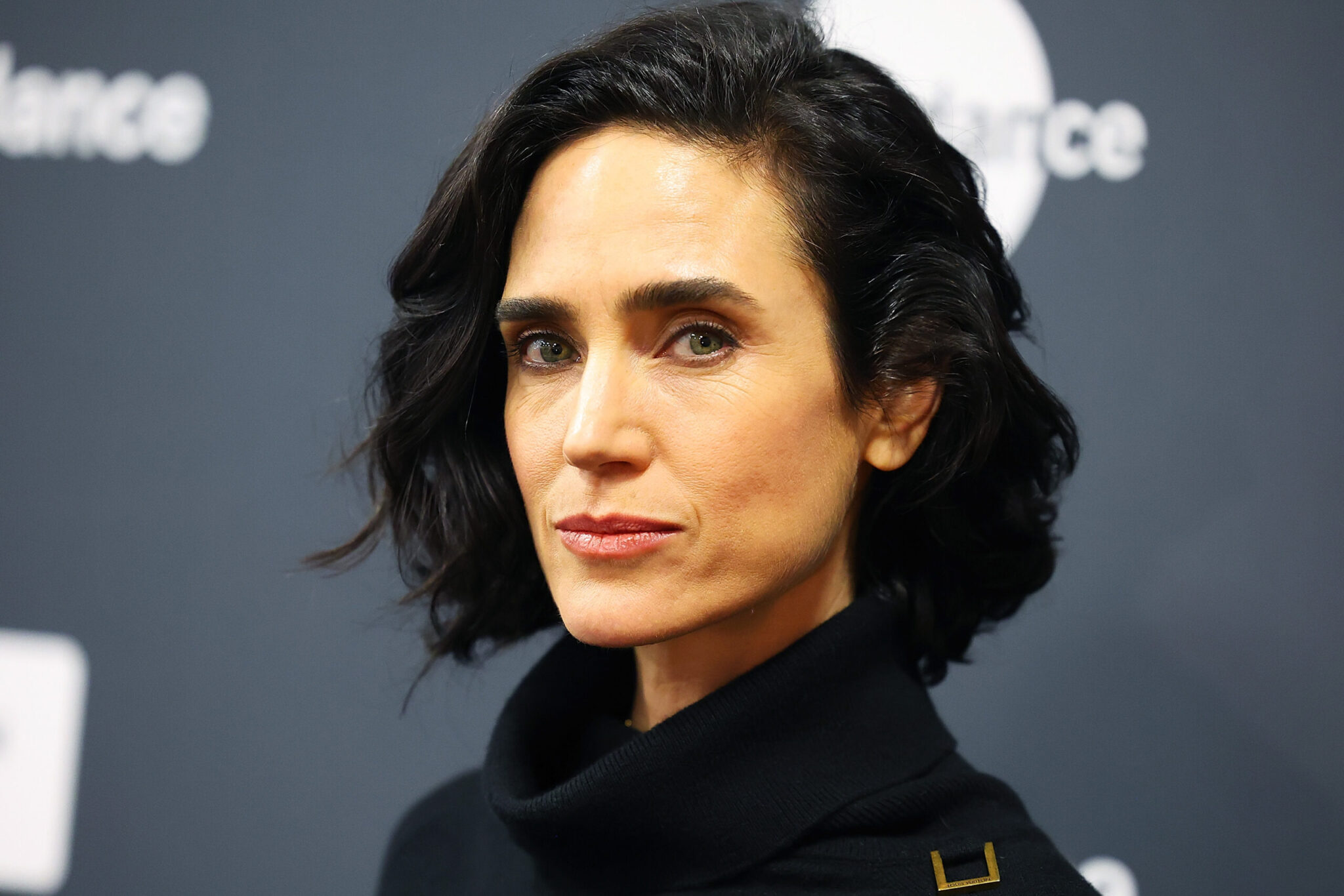 A woman with short black hair in a black turtleneck stares into the camera