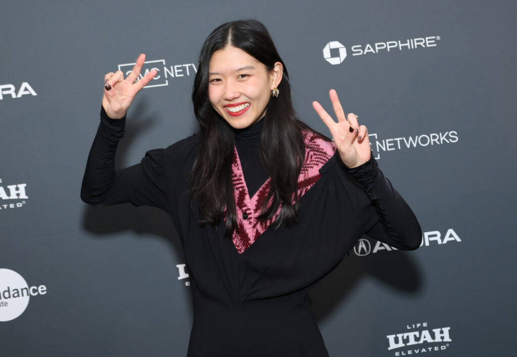 A woman dressed in black holds up peach signs in front of a step and repeat at the 2023 Sundance Film Festival.