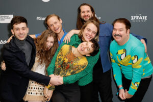The cast and crew of Mutt stand with their arms around each other in front of a step and repeat at the 2023 Sundance Film Festival.