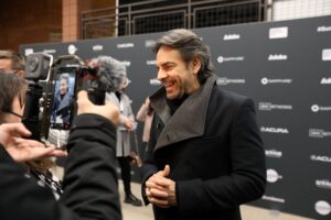 Man with graying hair and short beard smiles and laughs as he his photographed