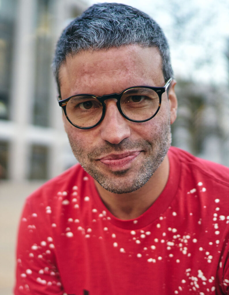 headshot of a man with glasses smiling in a red shirt looking at the camera