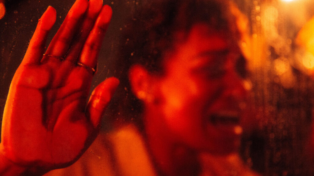 A young Black woman with short hair holds her hand up to a glass in distress