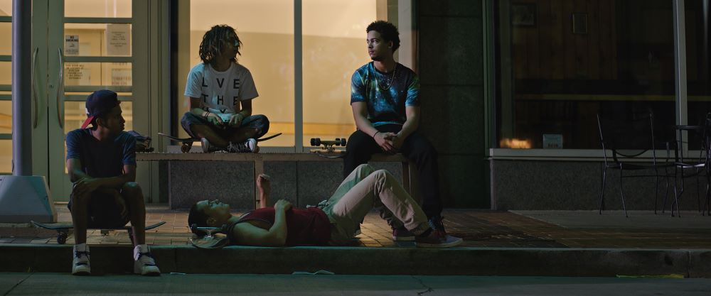 Four young men with skateboards hang out in front of what appears to be a storefront