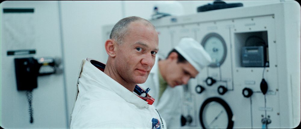 Man in spacesuit, with his helmet removed, smiles slightly