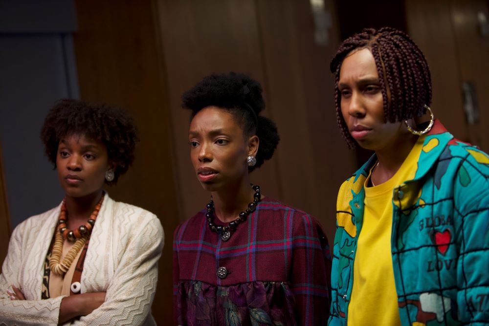 Three women stand shoulder to shoulder, looking critically at something to one side of the frame