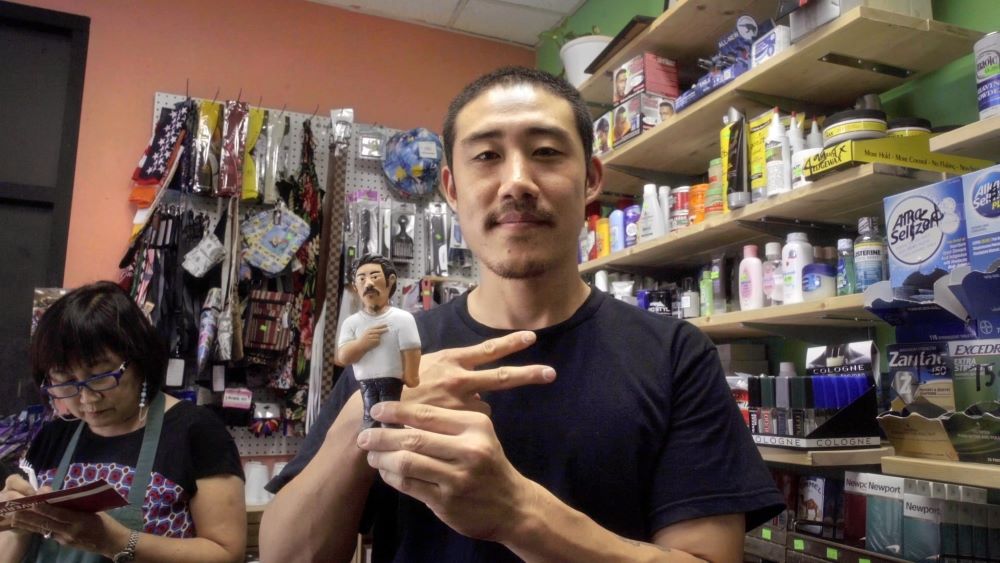 Young Asian man with mustache and slight goatee offers the peace sign in a store.